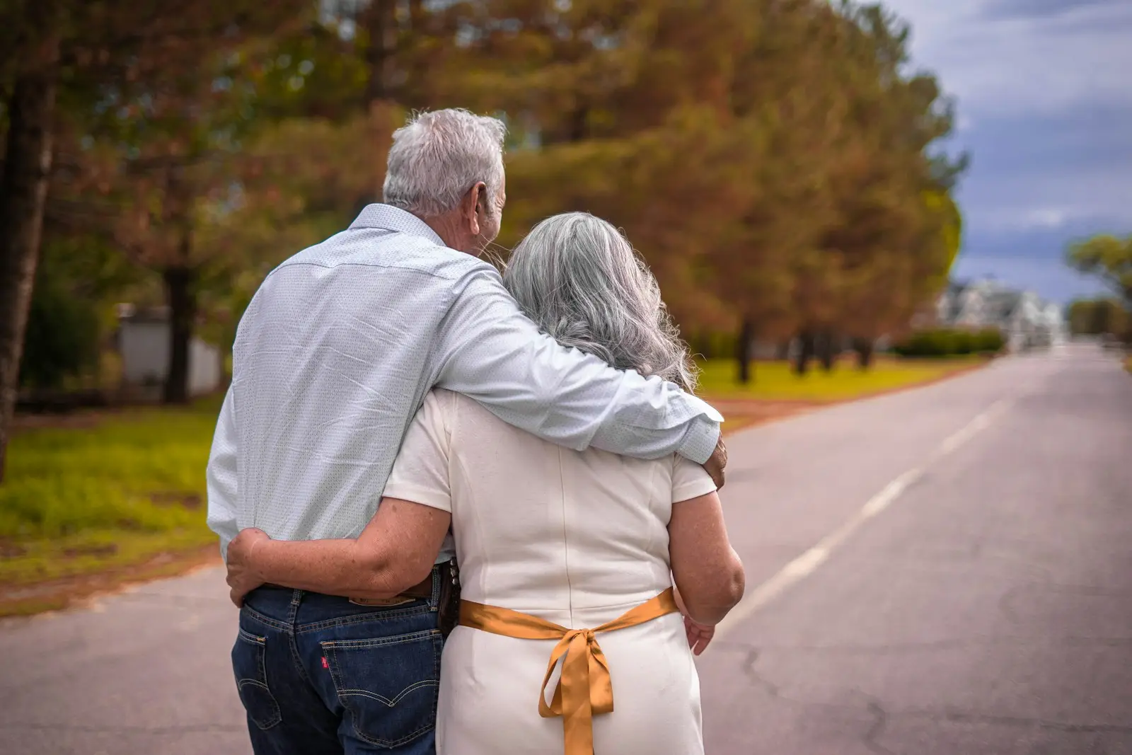 Pareja mayor paseando abrazada por un camino arbolado